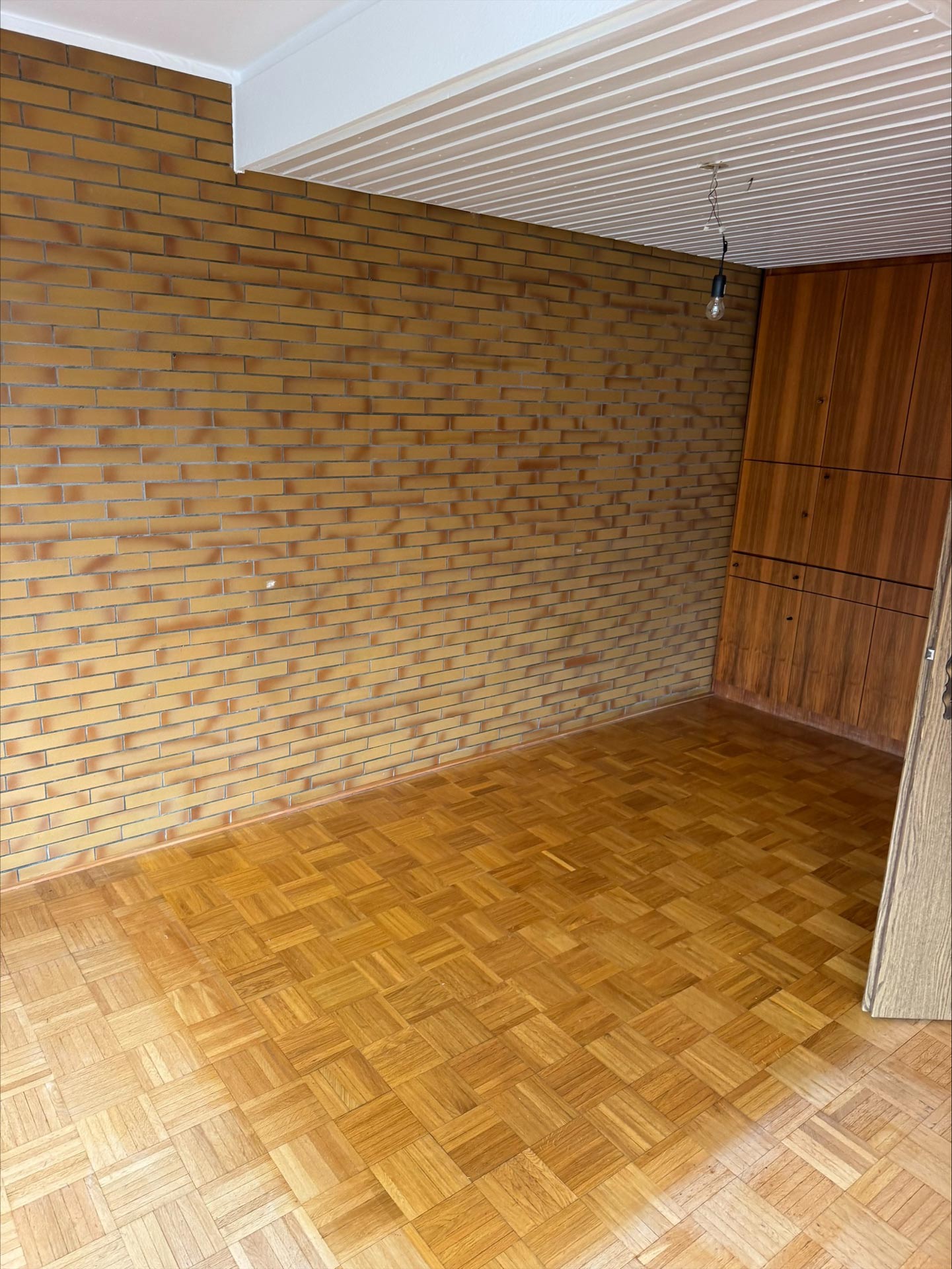 Ein leerer Raum mit brauner Backsteinwand, Parkettboden und Holzmöbeln
