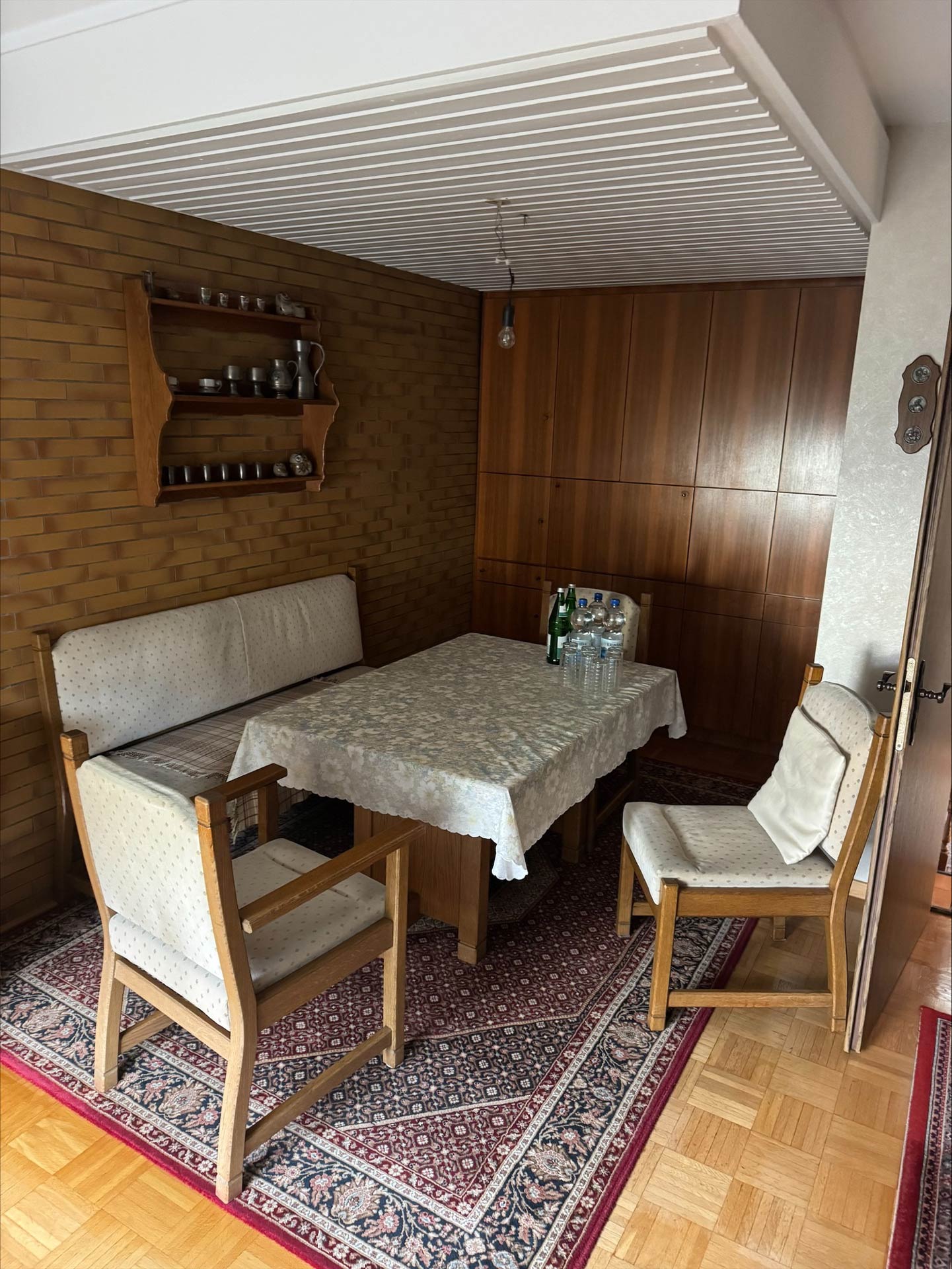 Ein Essbereich mit hellen Holzmöbeln, Teppich, Gläsern und grünen Flaschen
