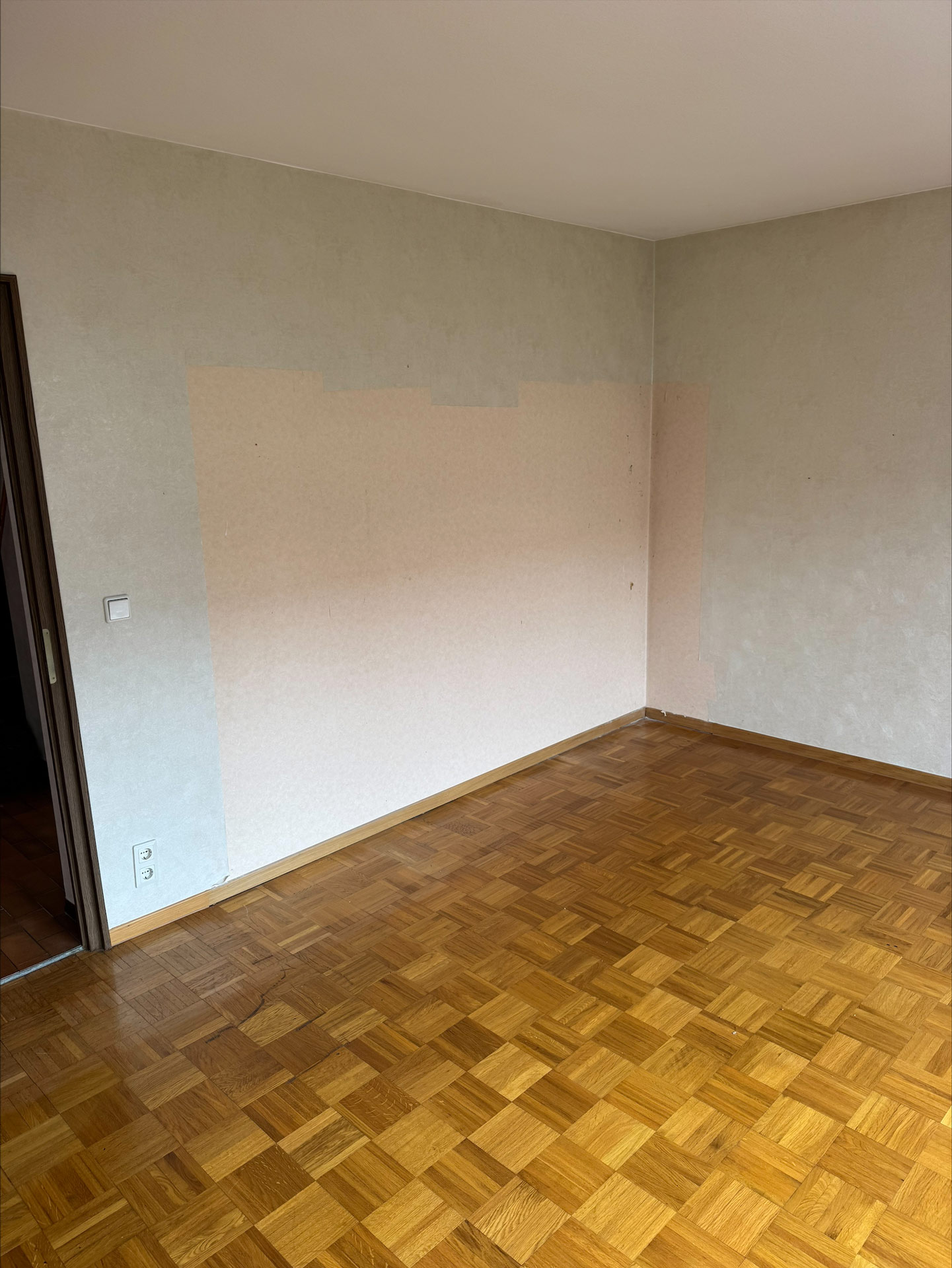 Ein leerer Raum mit Parkettboden, helle Wände und einer sichtbaren Farbfläche
