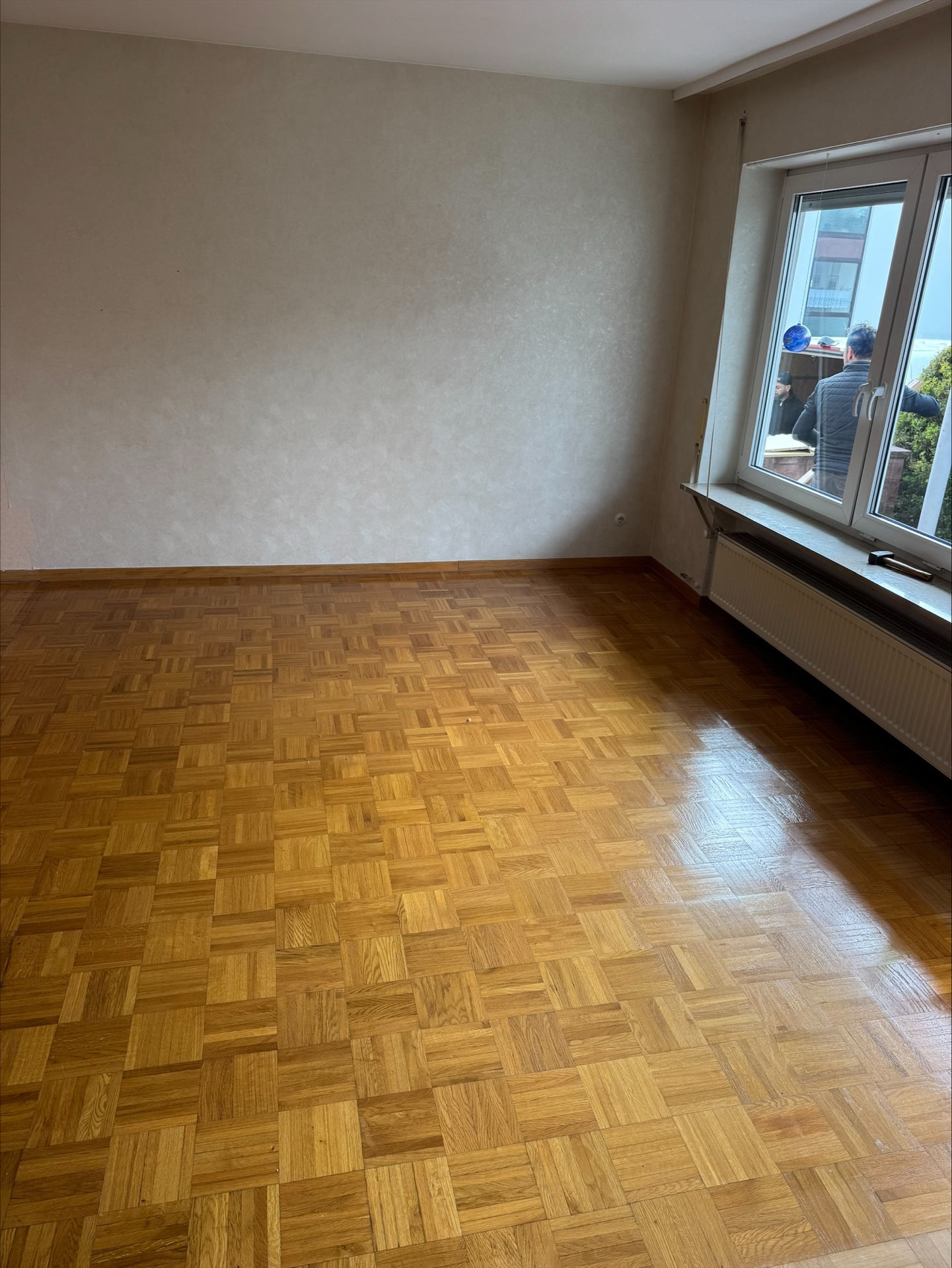 Helles Zimmer mit Parkettboden und zwei Personen draußen am Fenster mit blauen Hemden