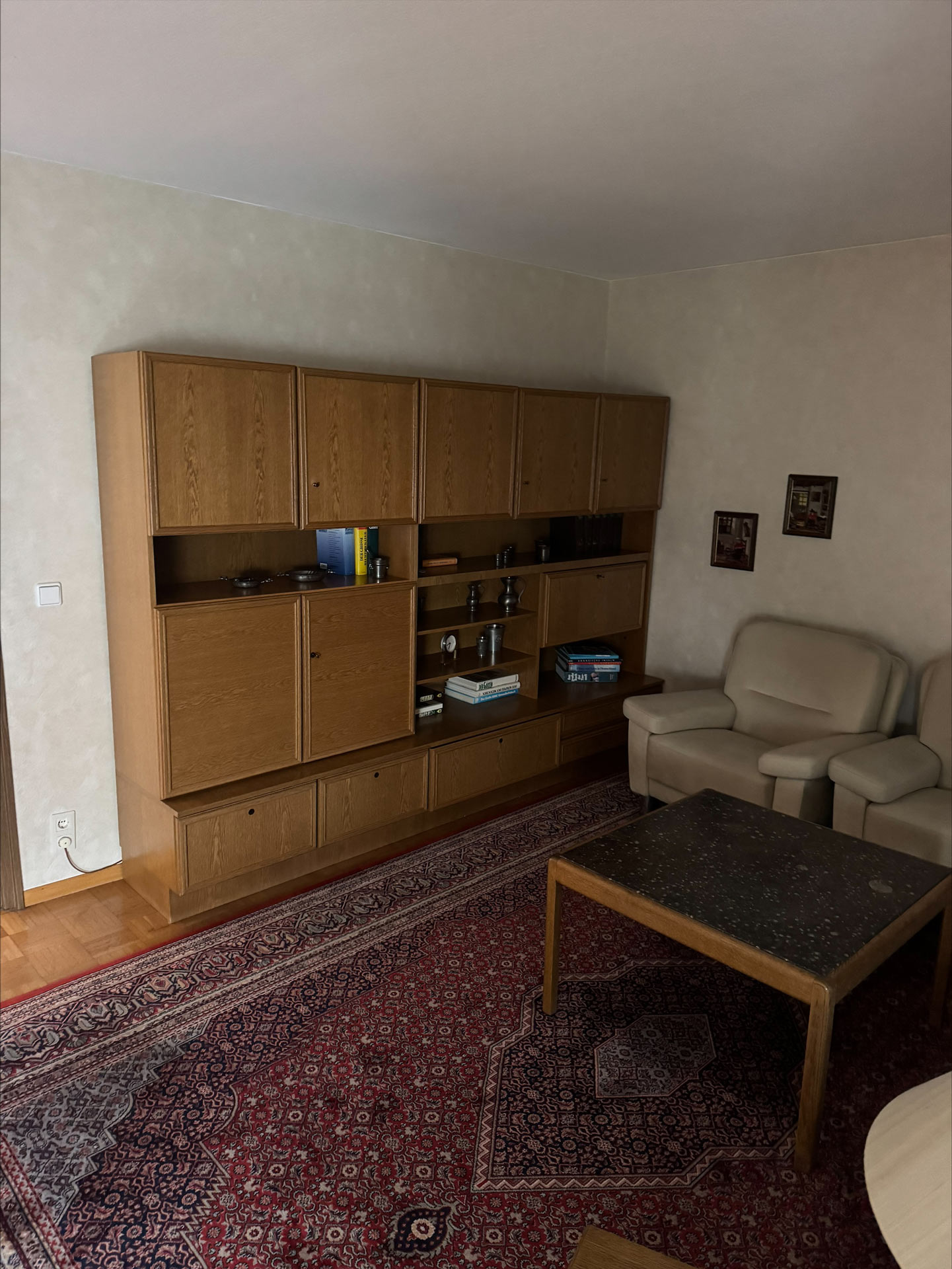 Ein Wohnzimmer mit Holzregal und beigen Sesseln in gedämpftem Licht
