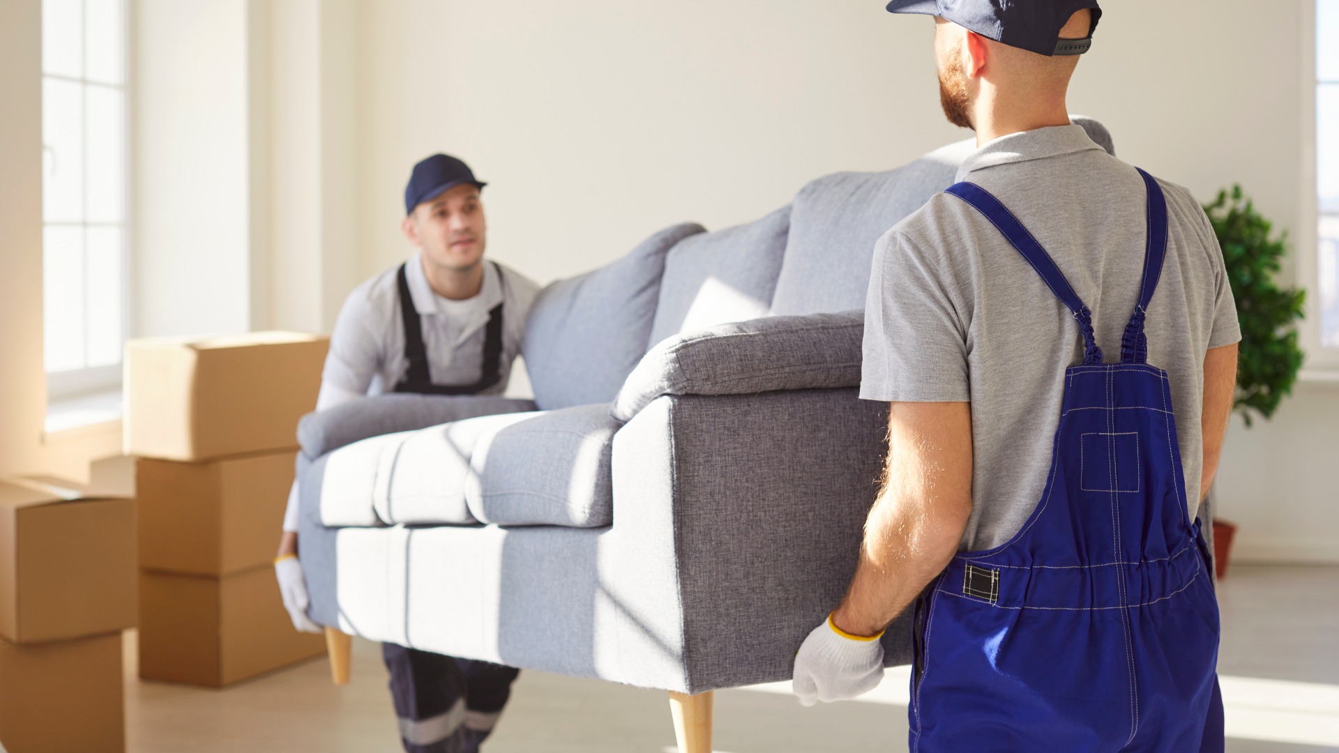 Two men movers carrying sofa from apartment, helping people to move to other place of living. Hard working workers from delivery service helping clients with relocation. Furniture delivery