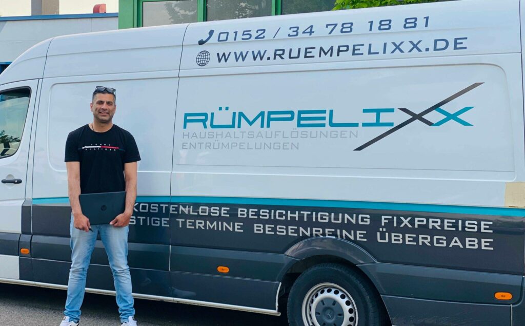 Lachender Mann in schwarzem Shirt vor weißem RÜMPELIXx Transporter mit blauen Logos